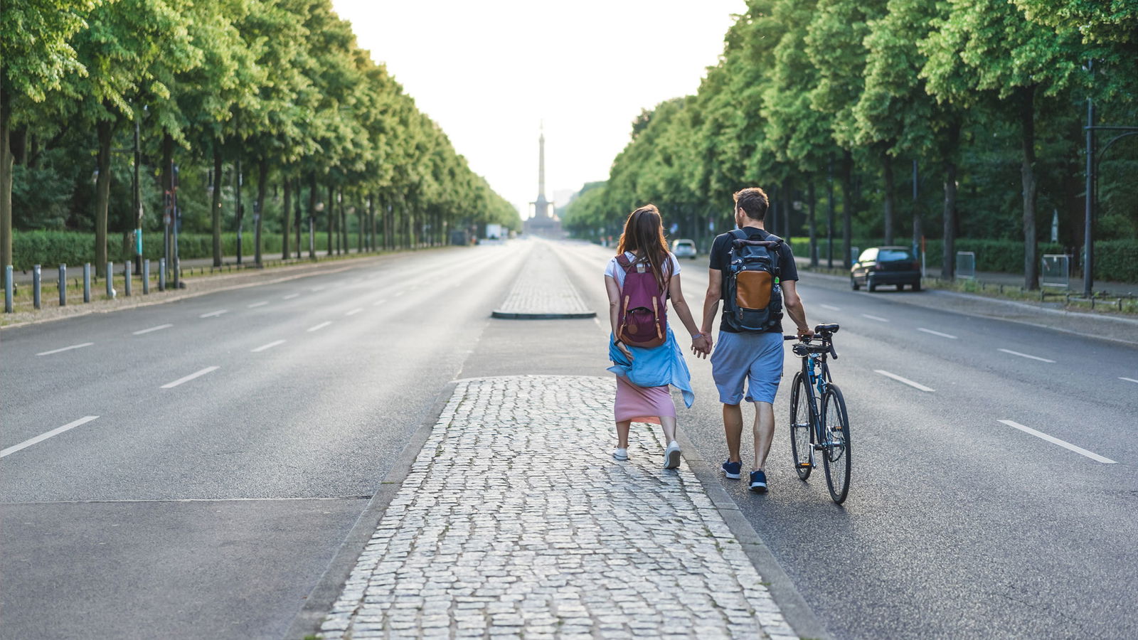 Siegessäule im Hintergrund mit zwei Touristen auf der Straße des 17. Juni in Berlin