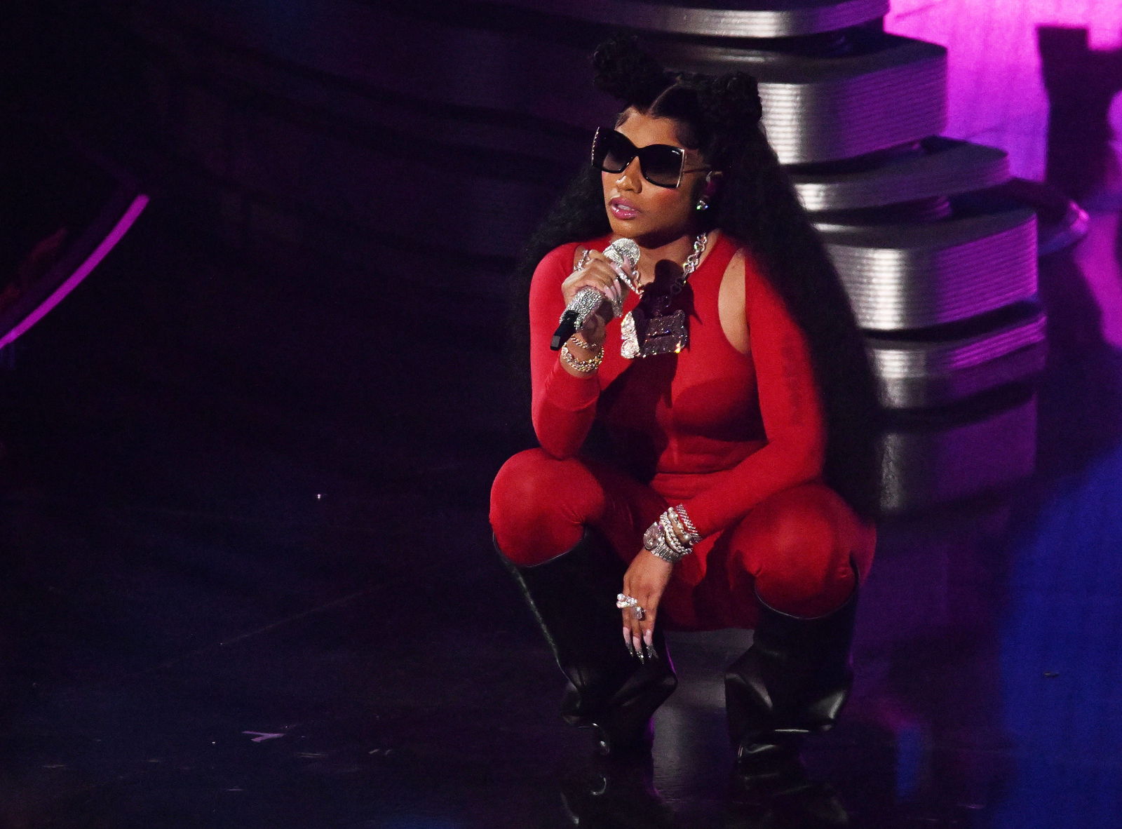 Künstlerin Rapperin Nicki Minaj hockt auf der Bühne in einem roten Einteiler und hat eine Sonnebrille auf