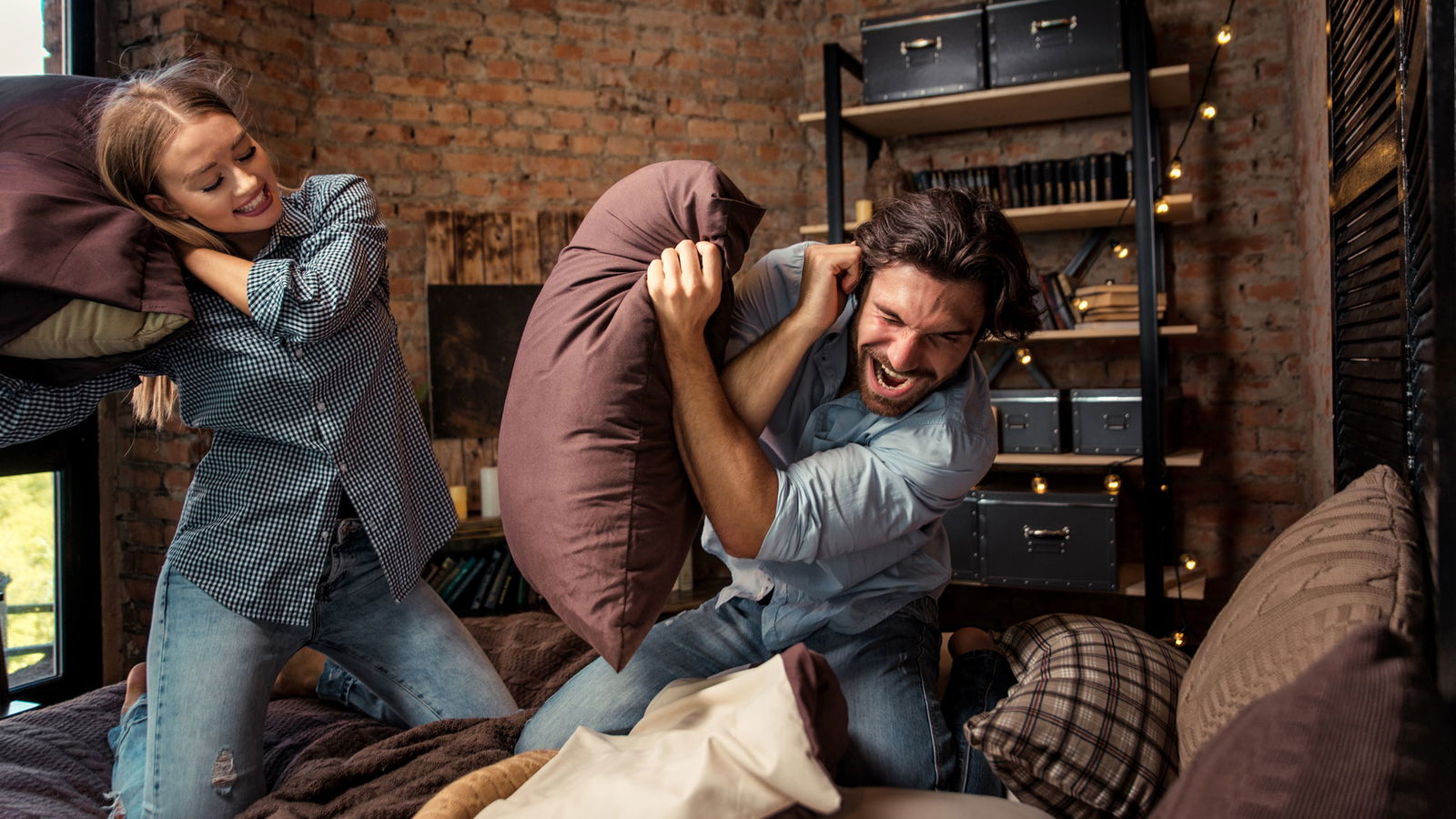 Paar auf dem Bett macht eine Kissenschlacht
