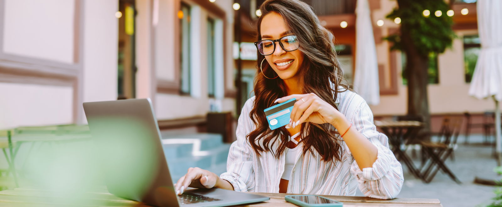 Frau am Laptop arbeitet draußen am Tisch mit Kreditkarte in der Hand