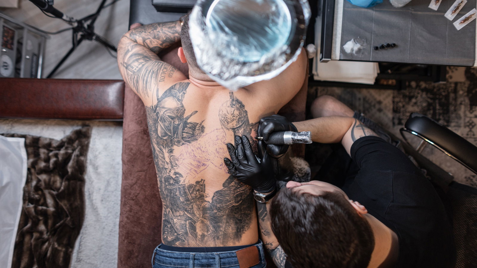 Mann liegt auf einer Liege im Tattoostudio und lässt sich den Rücken tätowieren